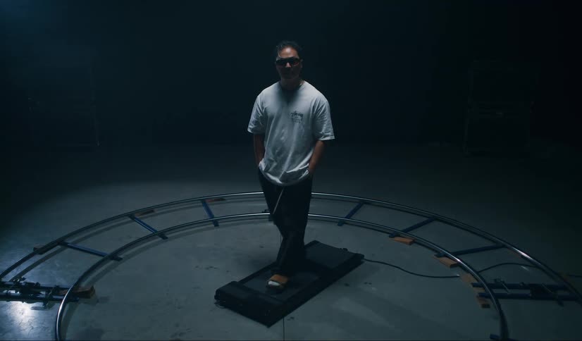 A man with hands in his pockets is walking on a small treadmill in a dark room
