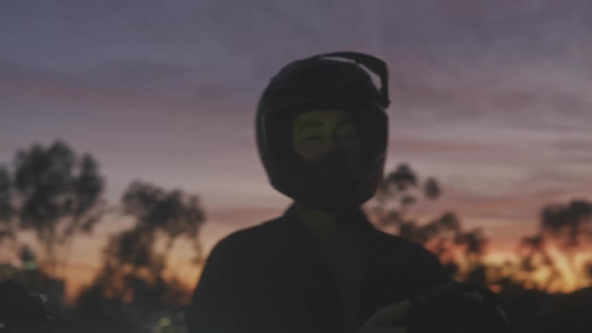 Man in helmet next to his motorcycle and with a metropolis in the background at sunset