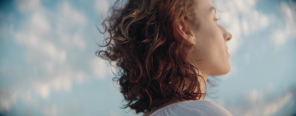 Redheaded woman stands outdoors staring toward the sky on a windy day