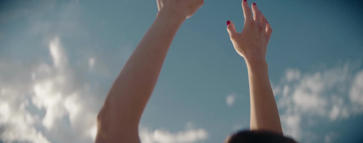 Woman with red nail polish raises her hands towards the cloudy sky