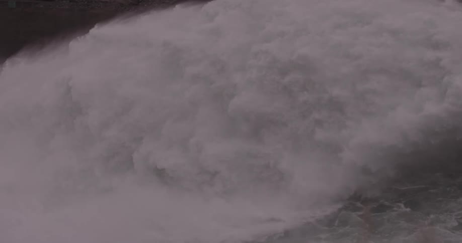 A massive flow of water pours out of a dam and into a river