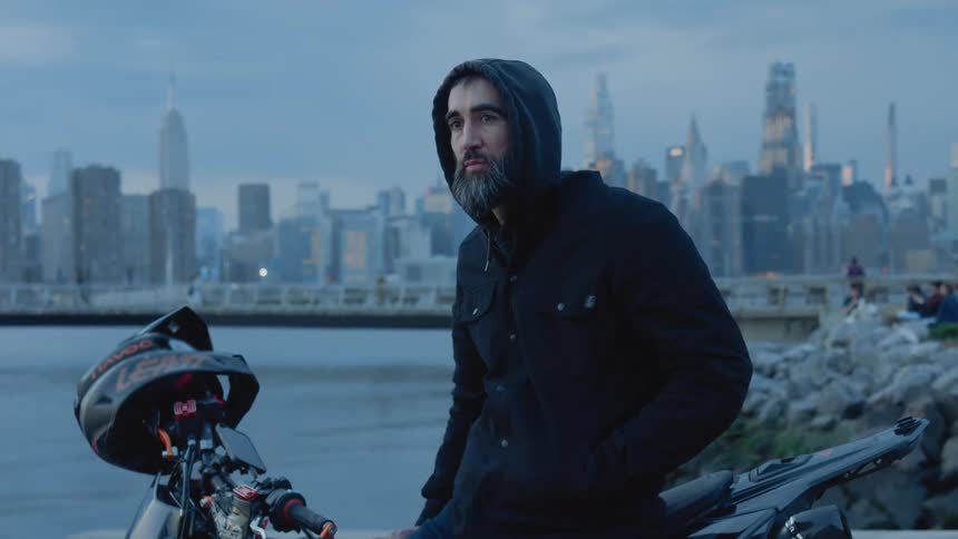 A man sits on his motorcycle by the shore