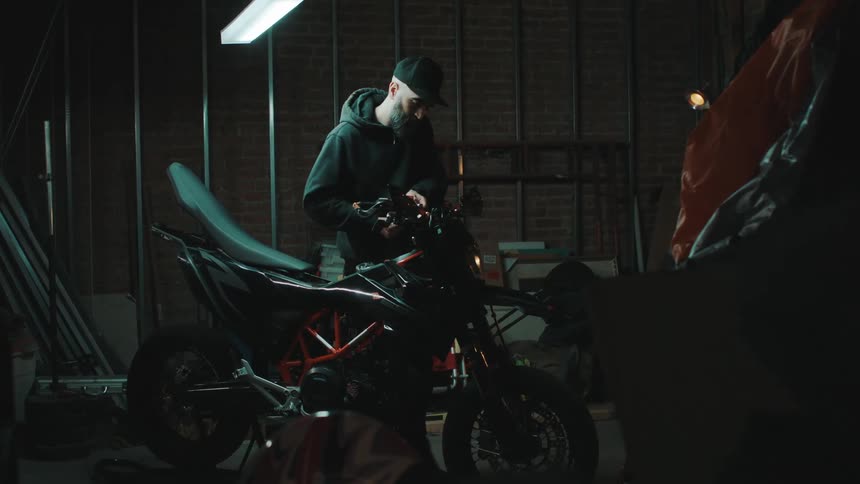 A man fixing up his black and red motorcycle inside of his garage