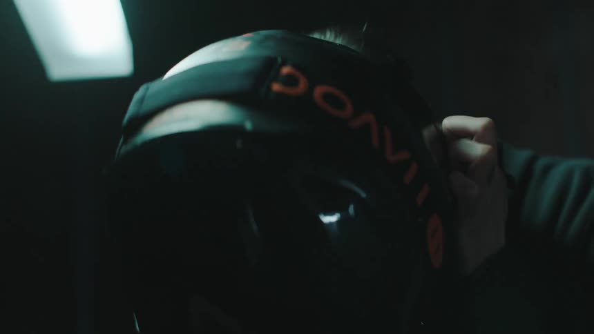 A person placing a helmet on their head in a dimly lit room
