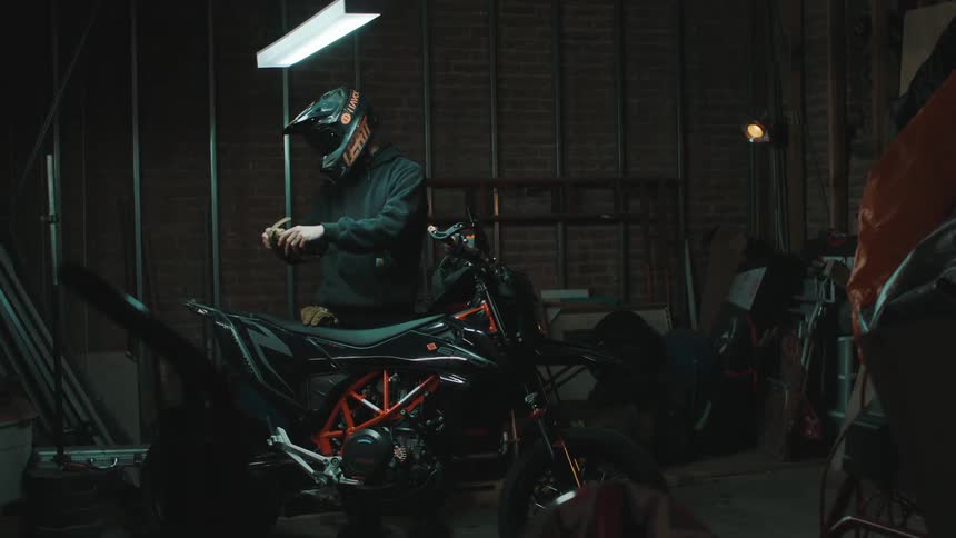 A person in a black coat is putting on a helmet and gloves and is in front of a motorbike