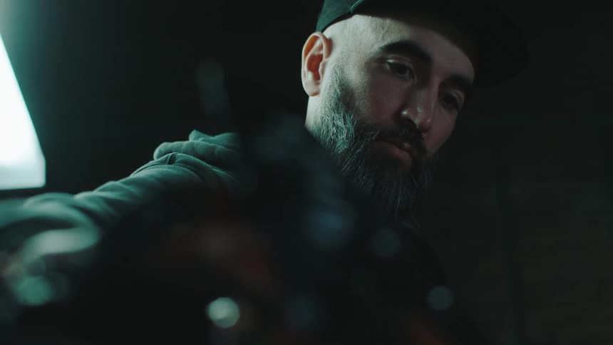 A bearded man in a black cap and black hoodie checks the motorcycle