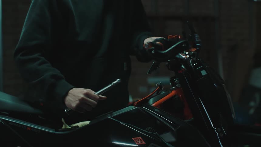 A male wearing a ball cap is tightening a handlebar on a bike