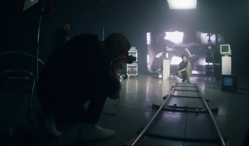 A man is crouched in front of a screen and two other men are taking photos of him