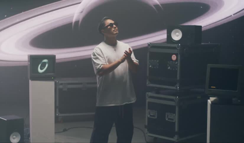 An individual stands between speakers inside a room in front of a projector