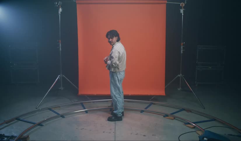 A man is posing showing his clothes in a dark room with an orange screen in the background