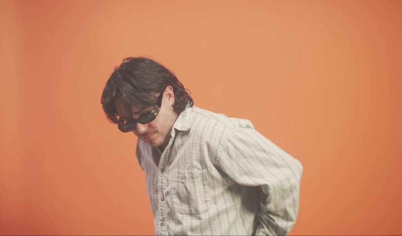 Man wearing sunglasses smiles while turning in front of a red backdrop