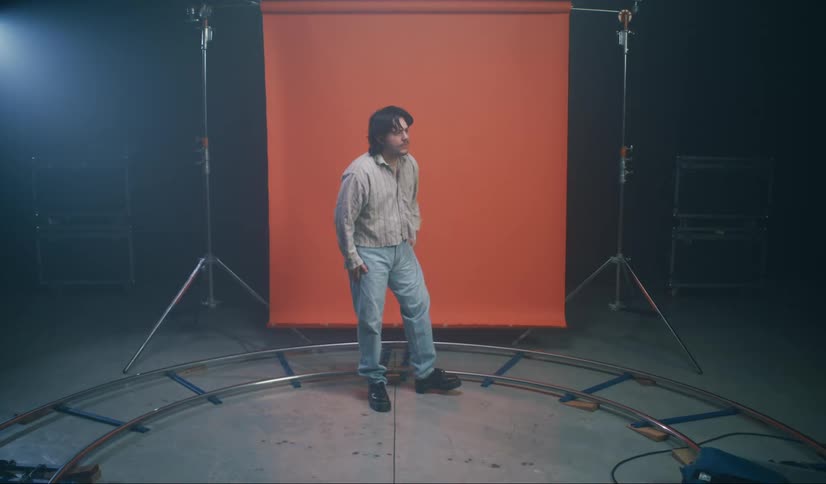 Man stands next to red backdrop in area surrounded by camera track on a set
