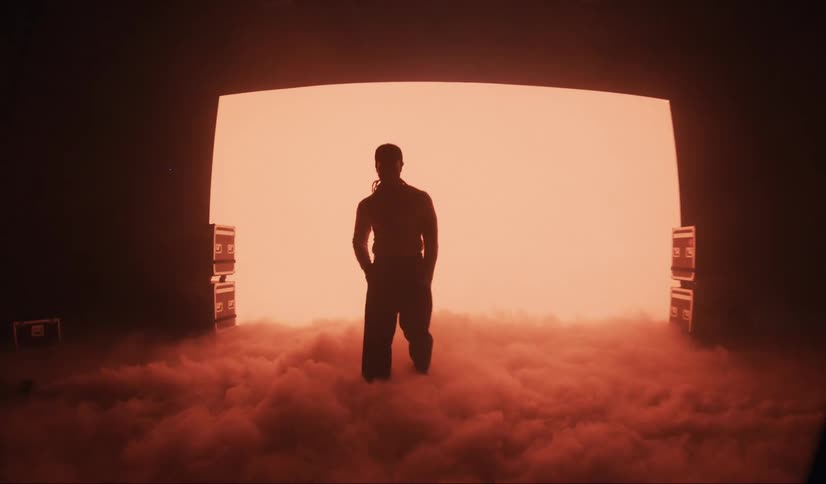 Man walking through smoke with a glowing screen in the background in a lowlit studio