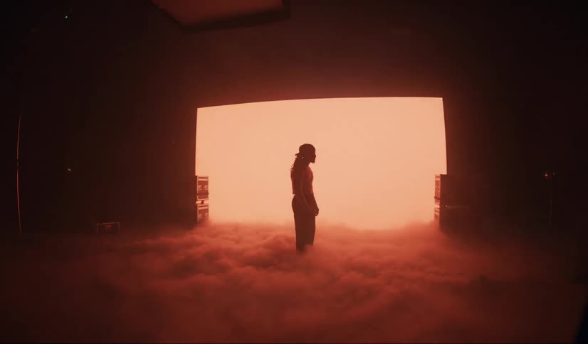A man is standing in the dark surrounded by smoke on the ground