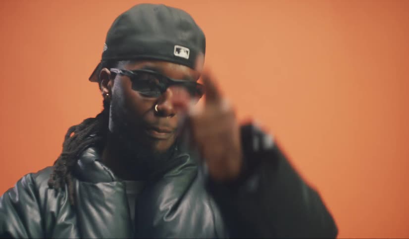 A man with sunglasses and backwards cap is making hand gestures and shaking his head met with an orange background