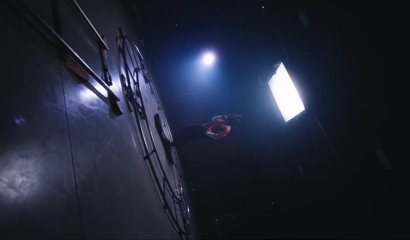 A person is walking on a treadmill that is wrapped around metal pipes in a dark studio with a light on top of the person