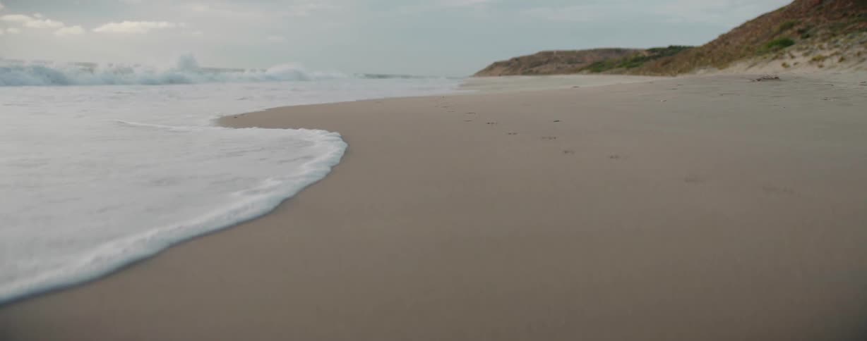 A beach with some smalls waves with foam reaching the sand