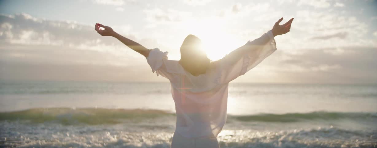 A woman is standing on the beach with her arms outstretched
