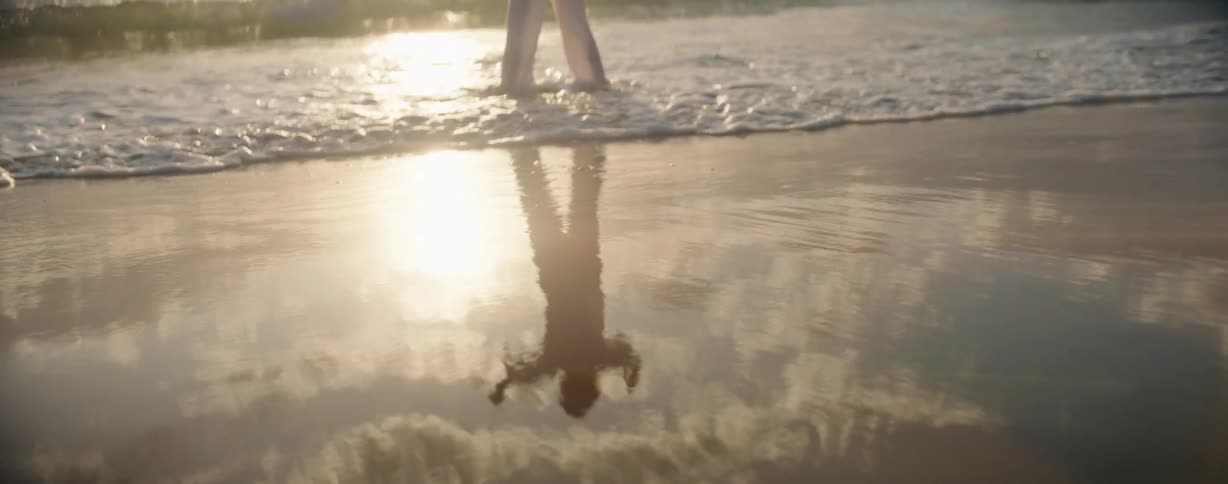Wet beach reflects person wading in the surf on a sunny day