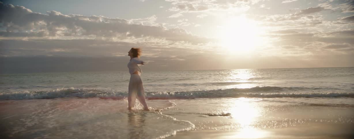 A woman twirls and splashes joyfully in the waves on the beach