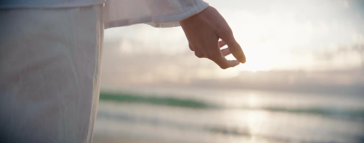 A woman who is wearing white clothes moving her hand in front the sun