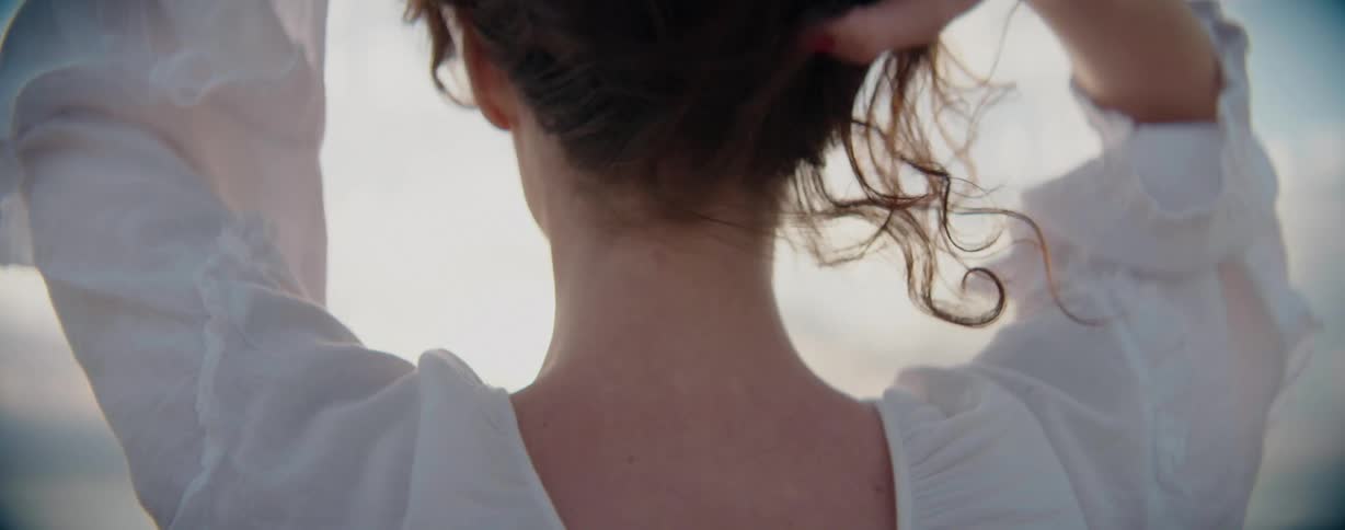 The back of a womans head who is holding her hair and she is wearing white clothing