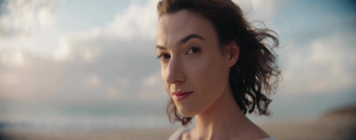 A woman smiles and looks at camera on the beach and walks off