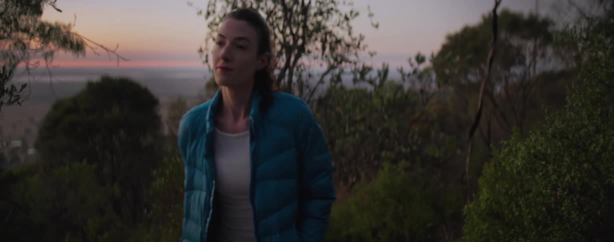 A woman hikes through a forest at sunrise