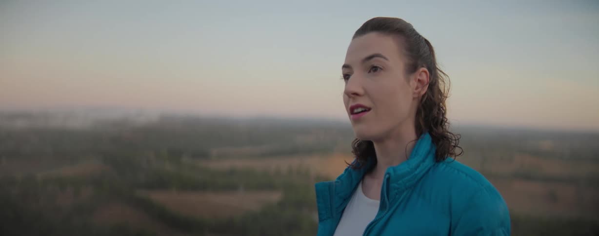 A woman wearing blue jacket is looking around in a nature environment