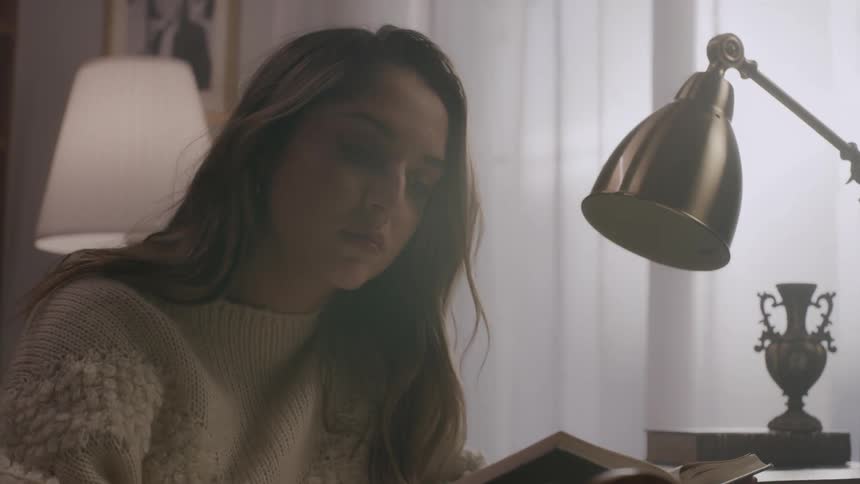 A young man and woman is sitting while reading a book and beside there is a lamp