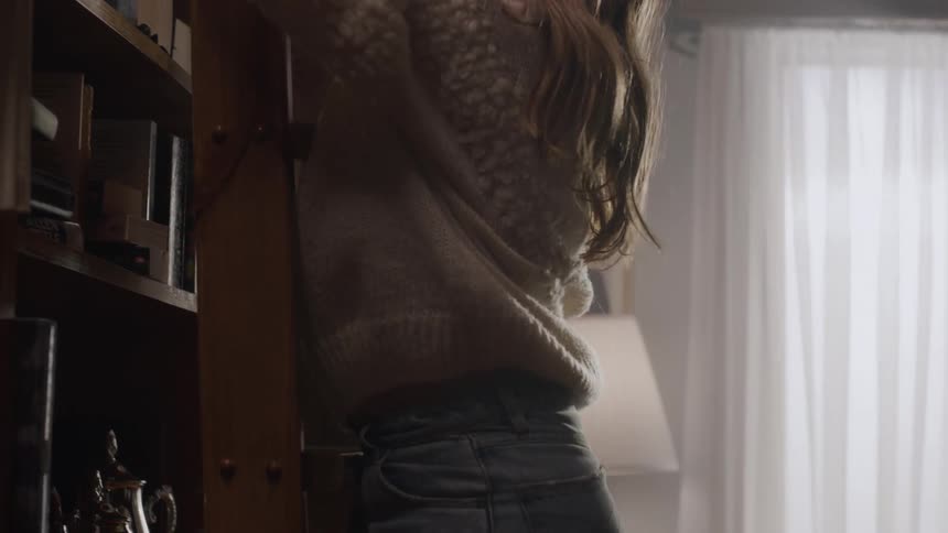 A young woman perches on a ladder reaching for a book on the shelf