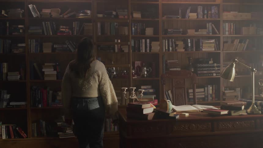 A female walks into a home library goes up on a ladder and grabs a book