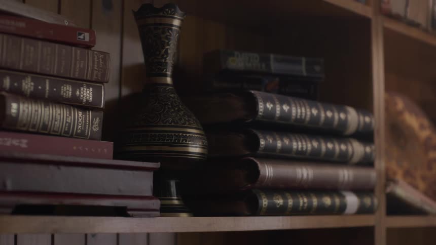 Closeup of stacked books and a black vase on a wooden library shelf