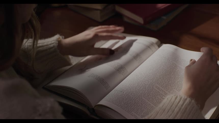 Blonde woman wearing a sweater turns the page of a book