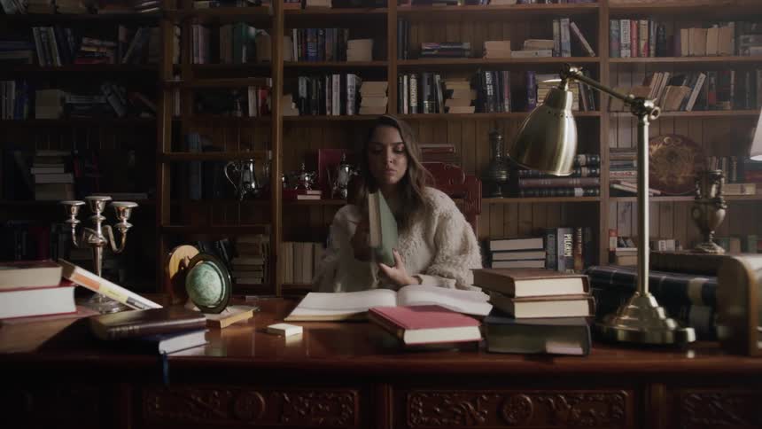 A young woman sits down at a desk and reads a book in a library