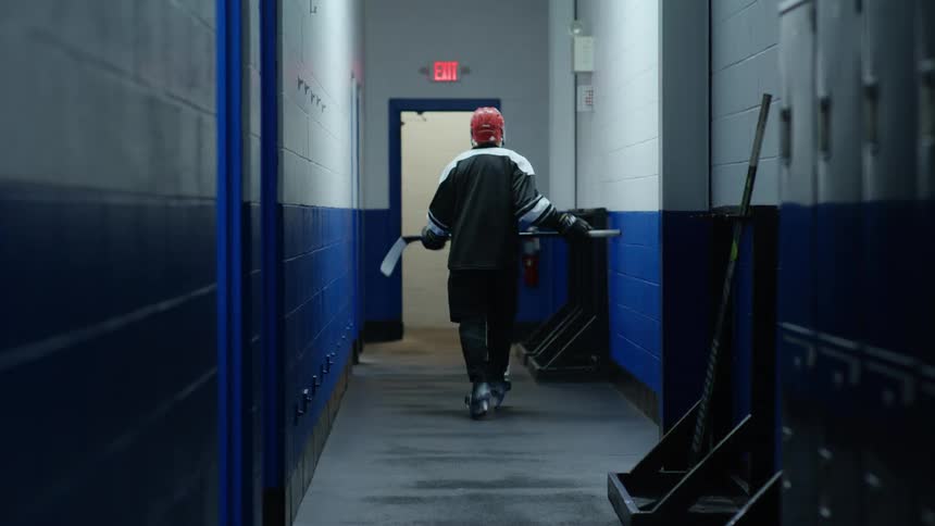 Young man leaving the locker room picking up his hockey stick and walking down the hallway