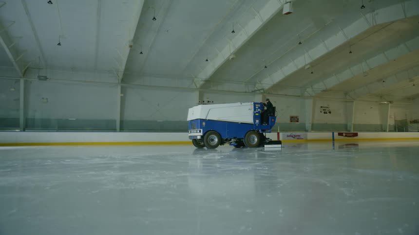 A man on a zamboni smoothing the surface of an ice rink