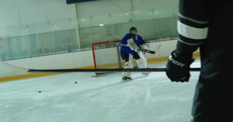 A group of hockey players taking turns to shoot pucks at a goalie