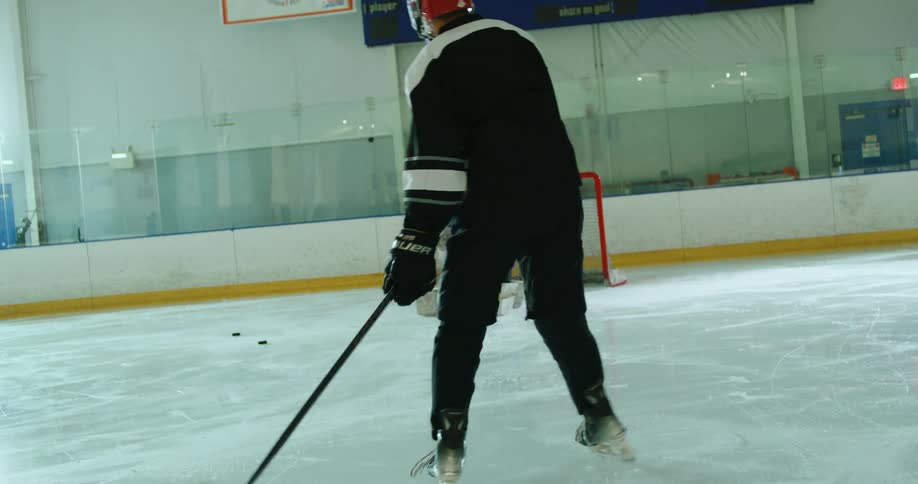 An indoor ice hockey rink with players taking turns to shoot at the goalie
