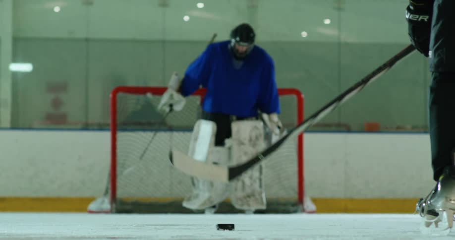A hockey player stands in front of the goal with another player in the foreground holding a hockey stick