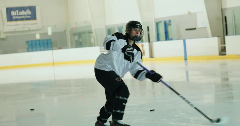 Woman with a hockey stick shooting pucks on an ice rink