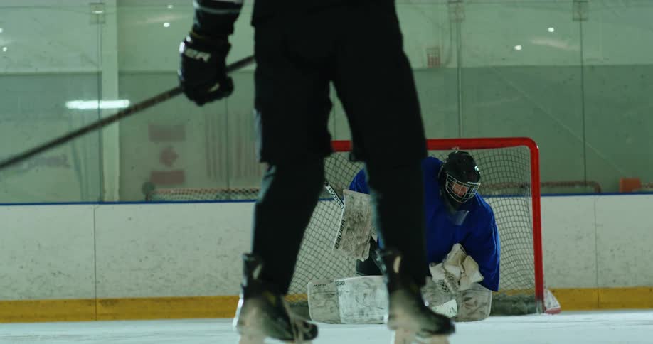 Person throwing a puck towards the goalkeeper with a stick on a hockey rink