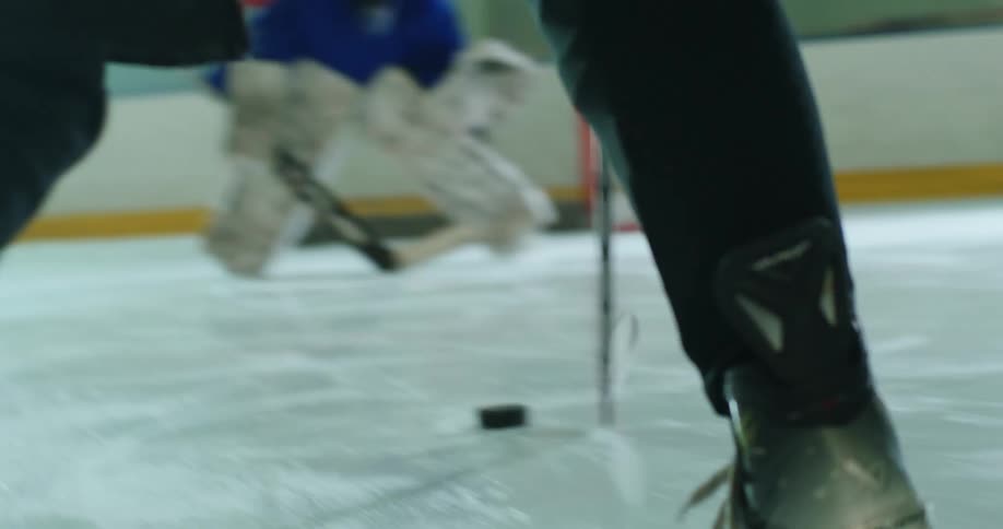 A hockey player chasing a puck aims for the goal on an ice rink