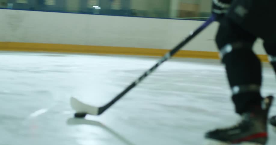 Person driving a puck with a hockey stick on an ice rink towards the goal