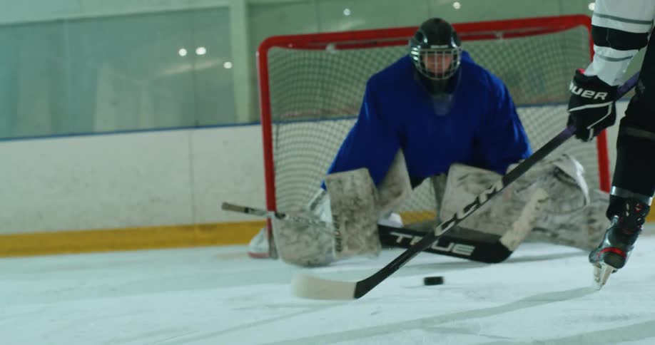 Person with a hockey stick throwing a puck towards the defending goalie
