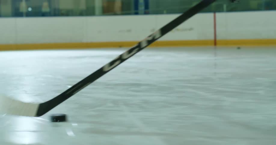 Person driving a puck in the sport of hockey on an ice court