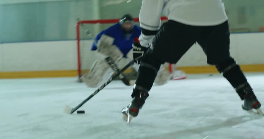 Ice hockey game with a player handling the puck with a stick towards another player in blue who is a goalie near the goal