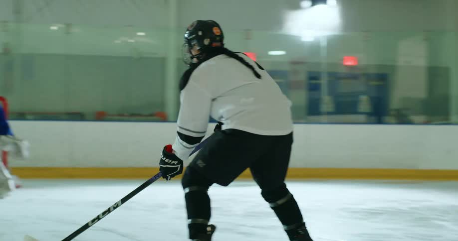 A hockey player takes a shot at a goalie standing ready to defend the net