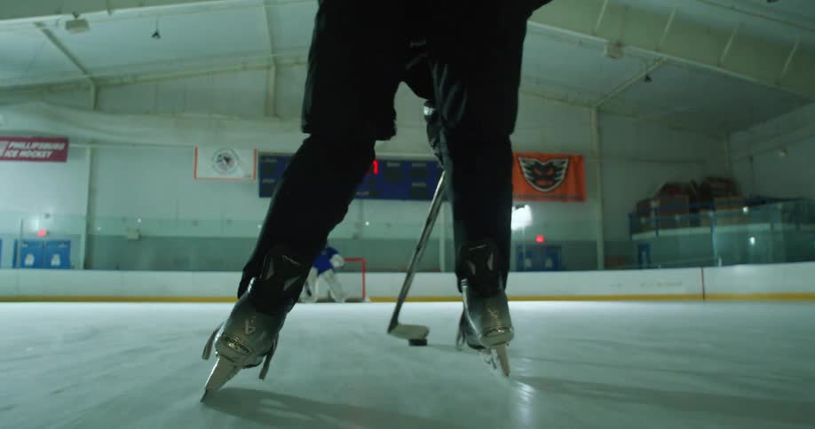 Player with a hockey stick handling the puck and attempting a goal against a goalkeeper