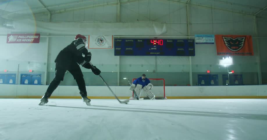 Hockey players pass the puck while quickly skating on ice and shoot towards a goalie who blocks it